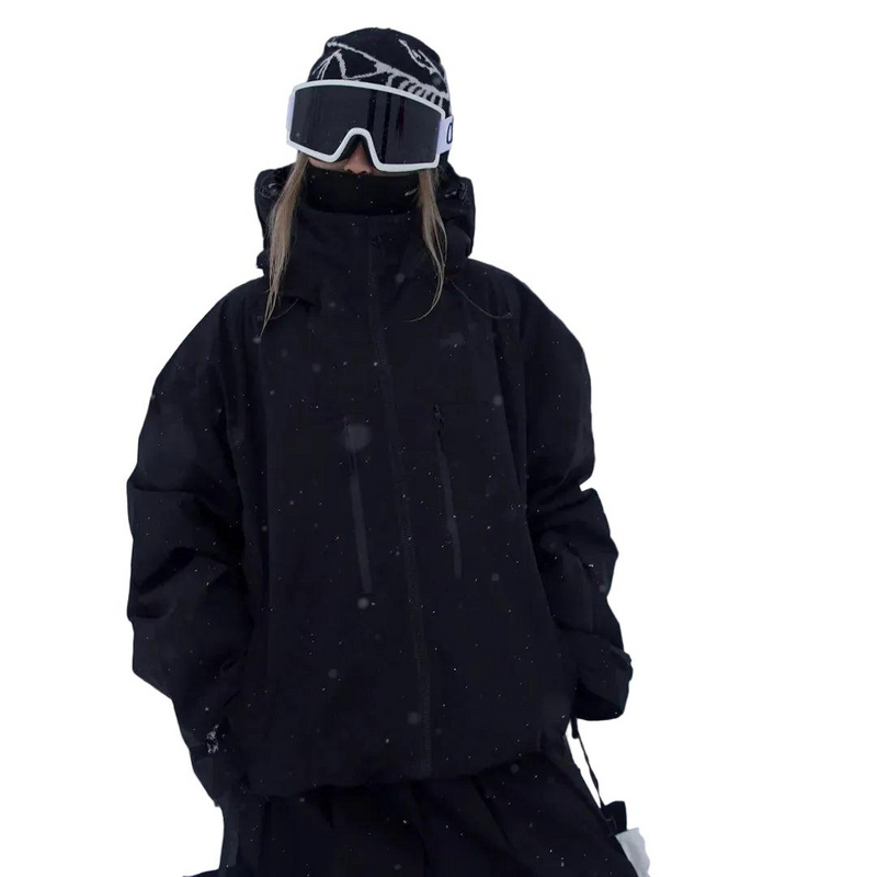 Person in schwarzer Schneejacke mit Stehkragen, Mütze und Skibrille, Frontansicht im Schneefall mit locker fallendem, weitem Schnitt. 3