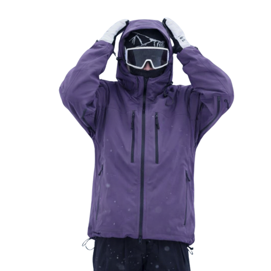 Person in violetter Schneejacke mit hochgezogener Kapuze und Skibrille, beide Hände am Kopf, Frontansicht mit zwei Brusttaschen und Kordelzug am Saum. 1