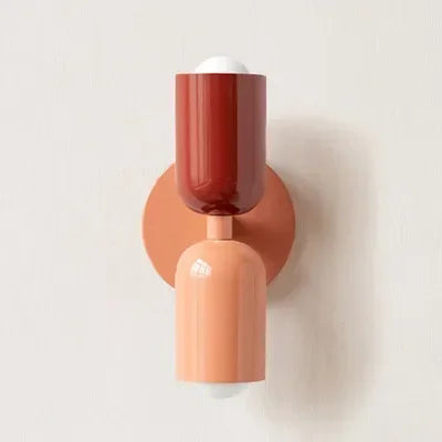 Einzelne Wandleuchte mit rotem oberem Schirm, rosa unterem Schirm und rosafarbener Wandplatte vor heller Wand. 20