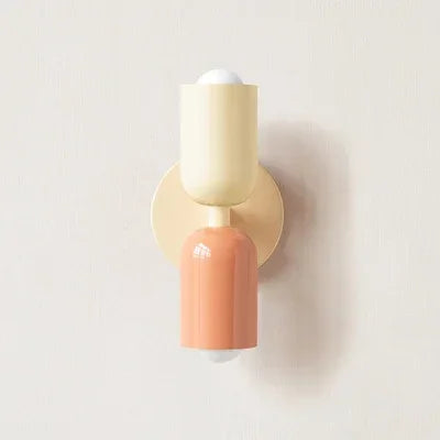 Einzelne Wandleuchte mit cremefarbenem oberem Schirm, rosa unterem Schirm und cremefarbener runder Wandplatte vor heller Wand. 16
