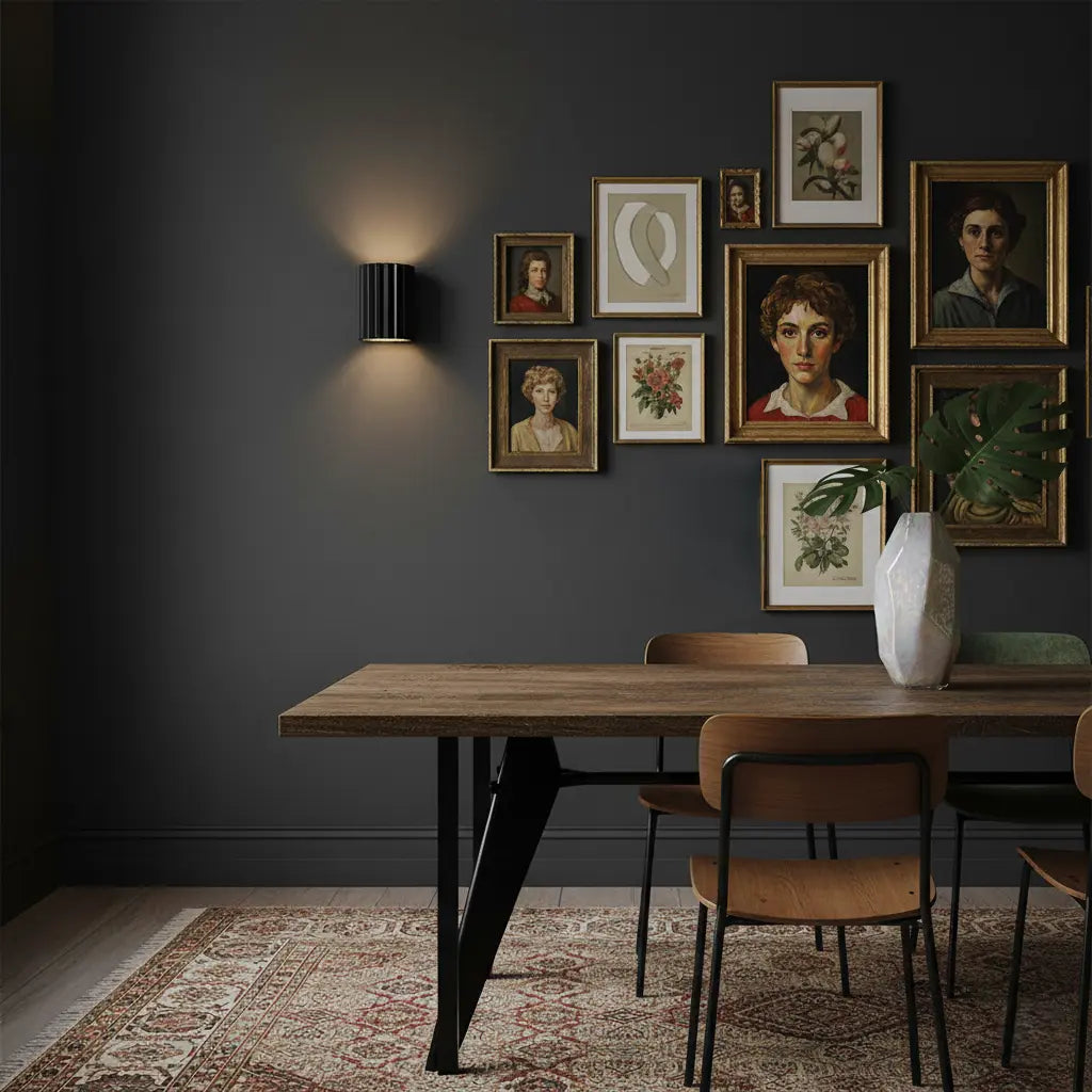 Schwarze gerillte Wandleuchte an dunkler Wand mit Bildergalerie über einem Holztisch mit Stühlen 6