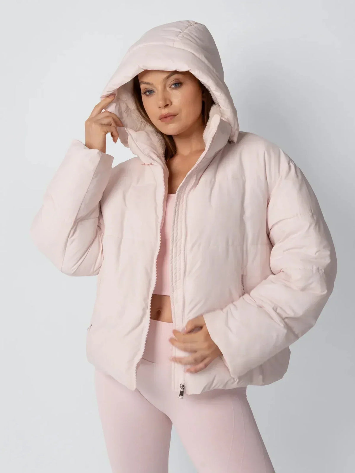 Model in der rosa Steppjacke mit übergezogener Kapuze, die Hand am Kapuzenrand 6