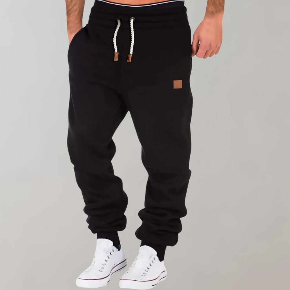 Schwarze Jogginghose mit weißem Kordelzug, getragen von einem Model mit weißen Sneakern, Hand in der Tasche 1