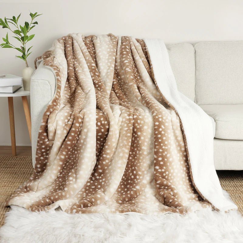 Braun-beige Decke mit weißen Punkten ist über ein helles Sofa drapiert, die weiße Kuschelseite hängt an der Seite herab. 1