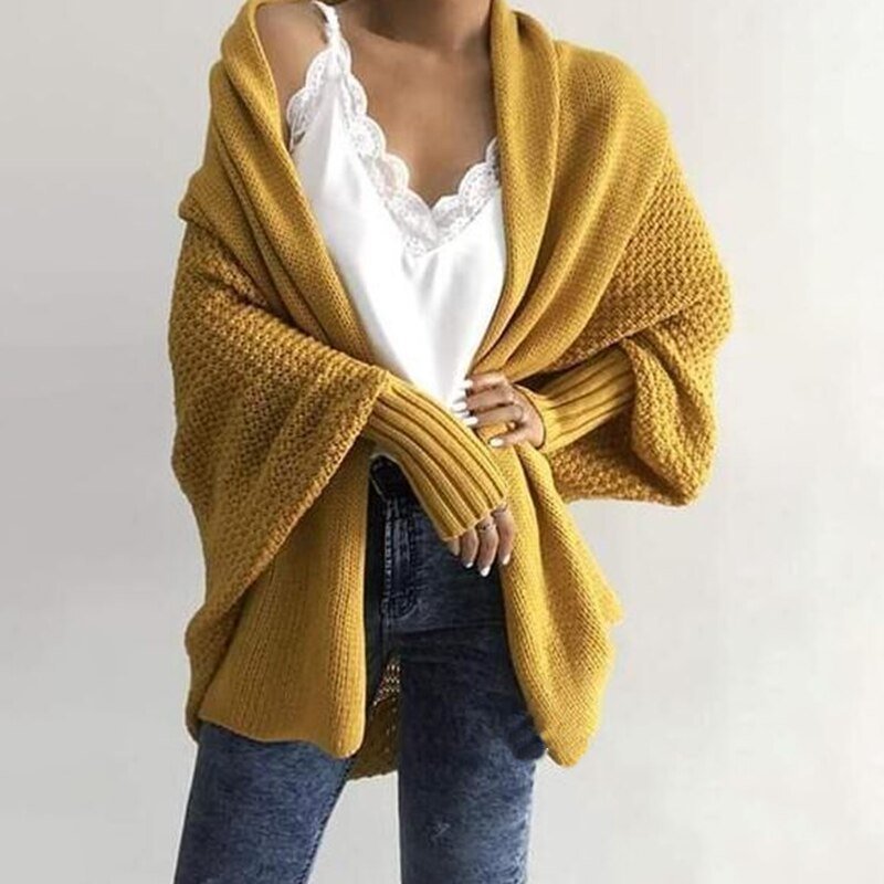 Frau in gelbem Strickcardigan, weißem Spitzen-Top und blauen Jeans, modisch, lässig.