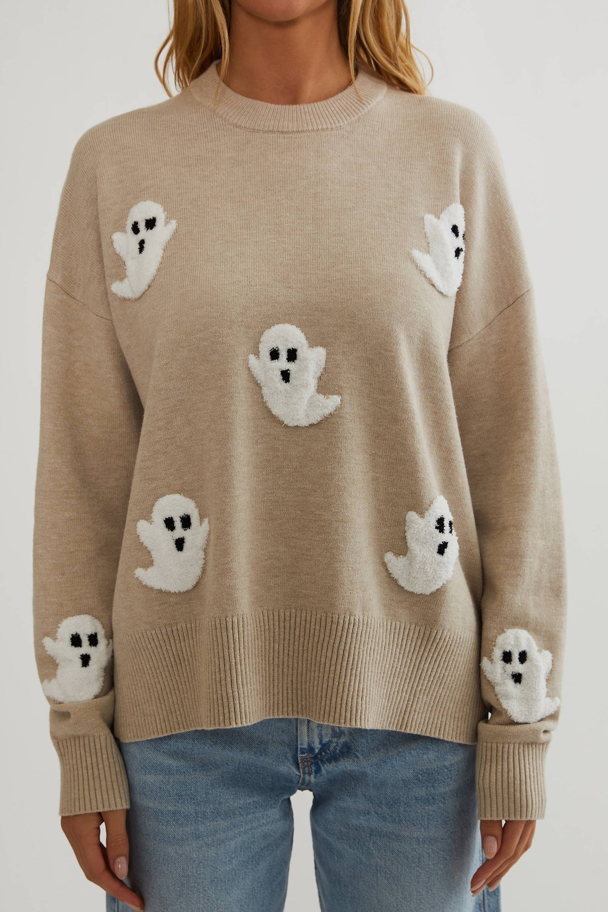 Nahaufnahme der Vorderseite des beigen Strickpullovers mit flauschigen weißen Geistern, Rippbündchen am Saum und an den Ärmeln. 2