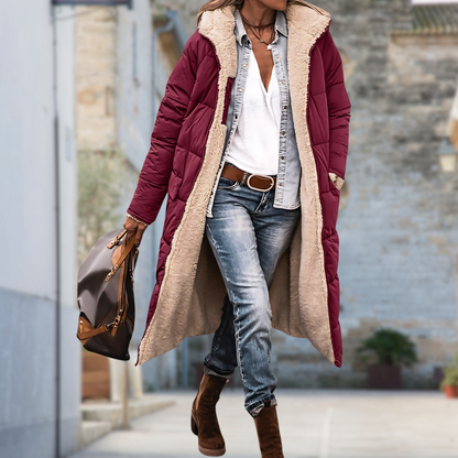 Frau trägt die weinrote lange Steppjacke offen mit hellem Teddyfutter, Jeans, braunen Stiefeln und Handtasche auf einer Gasse. 6