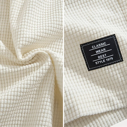 Zwei Detailaufnahmen in Creme: links die gewellte Waffelstruktur des Stoffs, rechts ein aufgenähtes schwarzes Stoffetikett an der Short. 9
