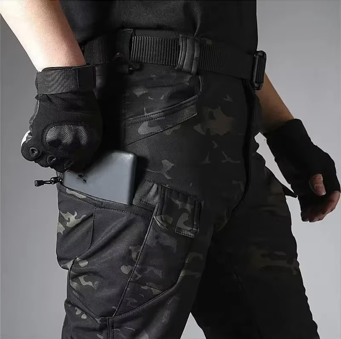 Detail der Camouflage-Hose am Model: Smartphone steckt in der Reißverschlusstasche am Oberschenkel, dazu Gürtel und schwarze Handschuhe. 19